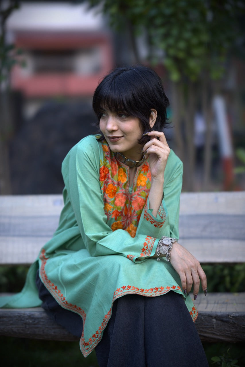 Woman sitting on a bench wearing a green traditional outfit with floral patterns.