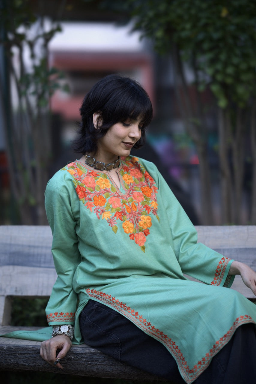 Woman wearing a green embroidered top sitting on a bench outdoors